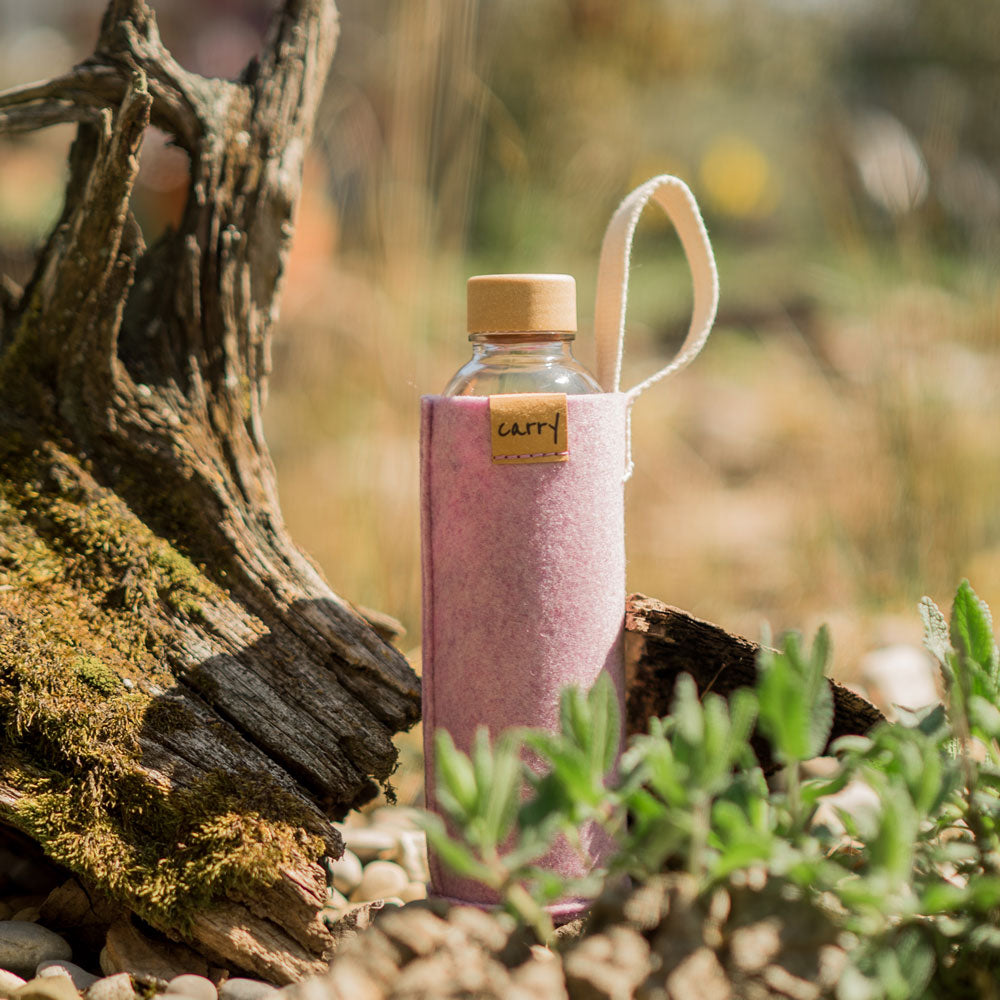 Rosa Filzhülle für Glastrinkflasche mit Trageschlaufe steht auf Baumstamm